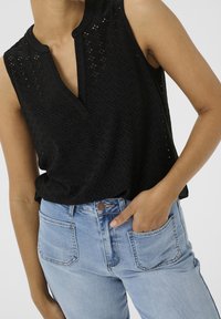 Haut noir sans manches avec un motif ajouré texturé, présentant un décolleté en encoche, associé à un jean taille haute bleu clair.