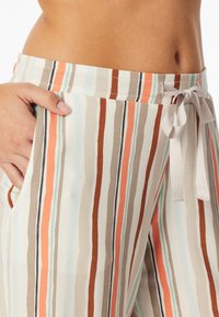 Pantaloni a righe beige, arancione e teal, con vita regolabile e tasche laterali. Tessuto leggero e morbido con righe verticali e texture liscia.