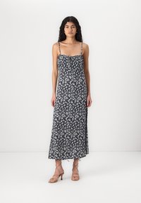 Rochie maxi floral de culoare albastru marin cu bretele subțiri, cu un corset plisat, material fluid și fante pe laterale. Poartă cu sandale cu toc de culoare bej.