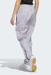 Pantalones ligeros de color púrpura claro, con cinturilla elástica, detalles de cremallera en los tobillos y bolsillos laterales, combinados con zapatillas blancas.