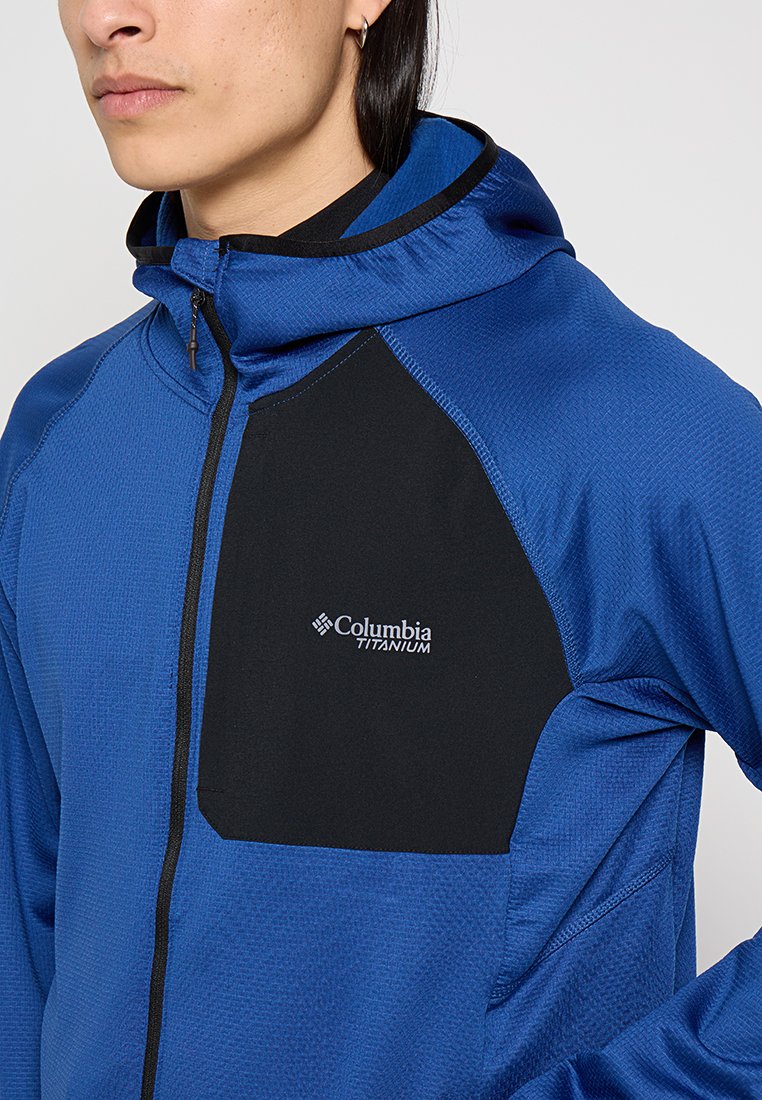 Veste à capuche bleue avec des accents noirs, dotée d'un tissu texturé, d'une fermeture éclair et du logo "Columbia Titanium" sur la zone de la poitrine.