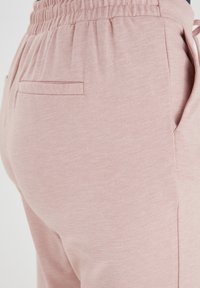 Jasnoróżowe spodnie dresowe wykonane z miękkiego materiału, z elastycznym pasem, pojedynczą tylną kieszenią i gładką teksturą.
