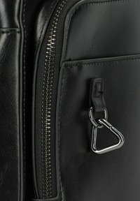 Schwarze Ledertasche mit texturierten Oberflächen, silbernem Reißverschluss und einem dreieckigen Metall-Schlüsselring, der an einem Leder-Ziehband befestigt ist.
