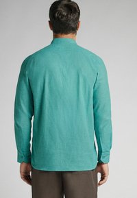 Turquoise langearmshirt made van gestructureerde stof, met een knoopsluiting bij de manchetten en een rechte zoom, gezien van de achterkant.