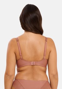 Soutien-gorge rose clair avec bretelles réglables, fermeture à crochets et œillets à l'arrière, tissu lisse et embellissements minimaux.