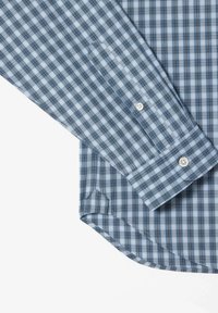 Camisa de cuadros azul y blanca, de botones y manga larga, con un dobladillo redondeado y botones blancos. La tela presenta una textura suave.