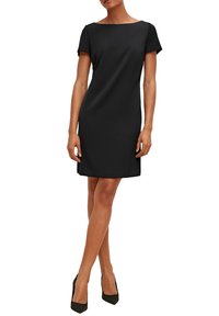 Schwarzes Kurzarmkleid mit einem Boots-Ausschnitt, aus glattem Stoff gefertigt. Klassische Silhouette, knielang, kombiniert mit schwarzen Absätzen.