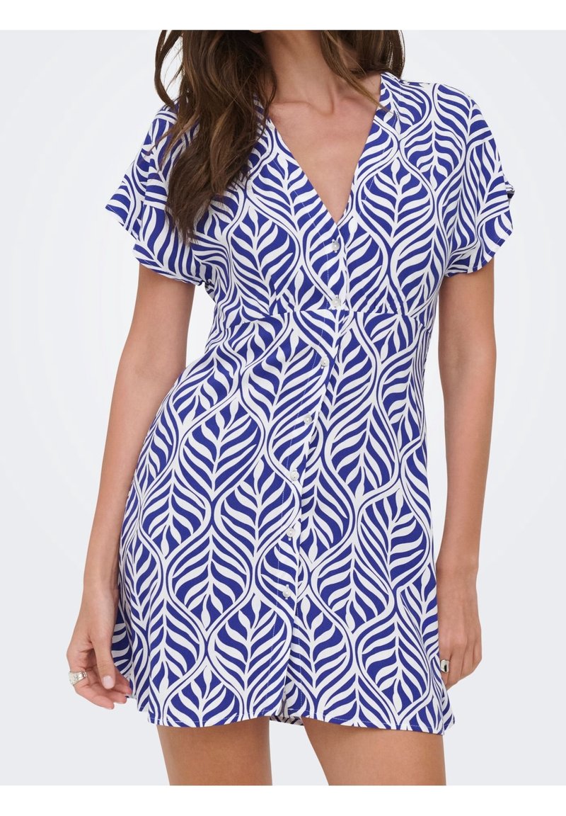 Femme portant une robe courte boutonnée à motifs bleus et blancs, manches courtes et col en V.