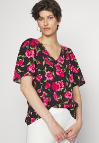 Blusa floral preta com flores rosa vibrantes e folhas verdes, com decote em V e mangas curtas, feita de tecido leve.