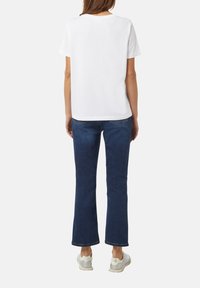 Witte katoenen T-shirt met korte mouwen, gecombineerd met blauwe flare jeans. Sneakers worden gedragen en het ontwerp is eenvoudig zonder patronen.