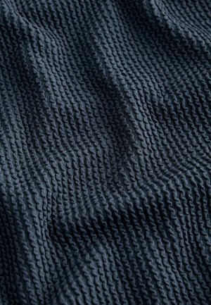 Kuvioitu, tummansininen kangas, jossa on aaltoileva malli ja kohotetut uurteet, esittelee pehmeän, neulotun ilmeen.