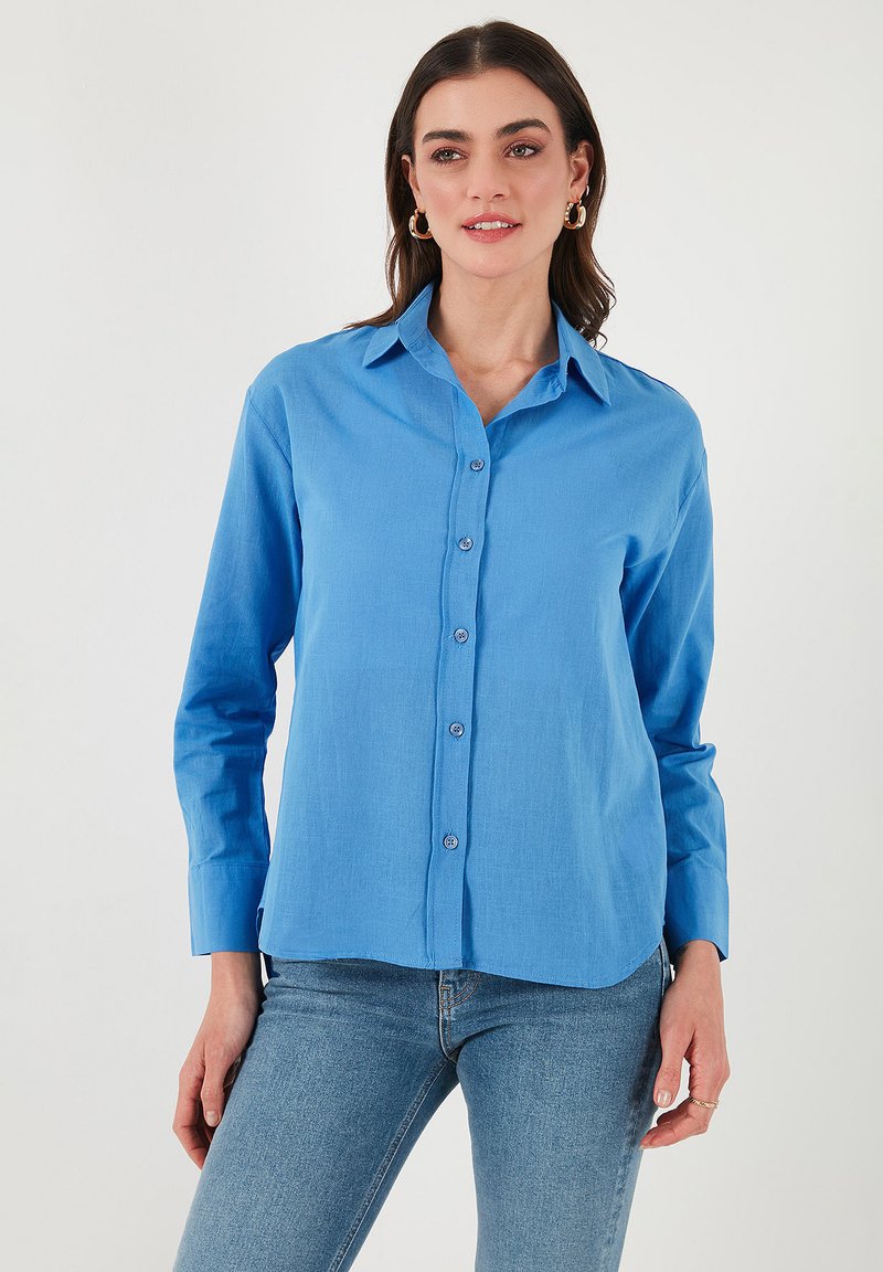Camicia button-up azzurra chiara con colletto classico, maniche lunghe e vestibilità rilassata. Tessuto liscio con leggera lucentezza e bottoni decorativi.