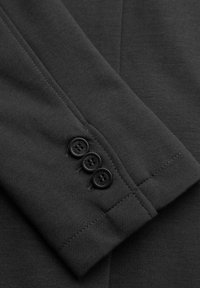 Manche de costume gris foncé avec trois boutons noirs cousus près du poignet, montrant une fine texture du tissu et des détails de couture.