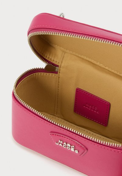 Ροζ δερμάτινη θήκη καλλυντικών με χρυστό φερμουάρ, με εσωτερικό σε ταμπά απόχρωση και ετικέτα με ανάγλυφη επιγραφή "MARC JACOBS." Λείο υλικό και δομημένος σχεδιασμός.