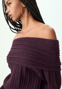 Burgundy ribbed neule off-shoulder med bred, teksturert halsutskjæring og lange ermer, laget av et mykt, varmt stoff.