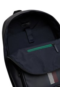 Zaino navy con un'esterno liscio, una tasca frontale con zip verde e un interno caratterizzato da un'etichetta e una fodera in tessuto.