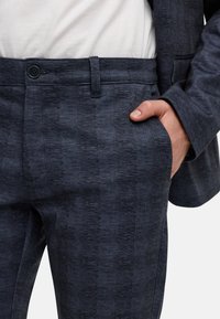 Granatowe spodnie garniturowe w kratę wykonane z teksturowanej tkaniny, z zapięciem na guzik i bocznymi kieszeniami, o dopasowanym kroju.