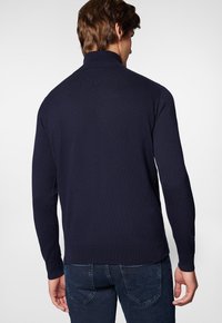 Granatowy sweter dzianinowy z podszyciem, długimi rękawami, ściągaczami przy mankietach i dolnym brzegu, charakteryzujący się gładką fakturą i dopasowanym krojem, widoczny z tyłu.