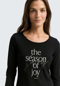 Black long-sleeve t-shirt featuring the text "the season of joy" in white with decorative accents. Smooth fabric, crew neckline, and relaxed fit.