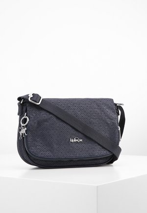 Czarna torebka na ramię z wzorem, regulowanym paskiem, zamknięciem na zamek i srebrną zawieszką w kształcie małpki, na białym tle.