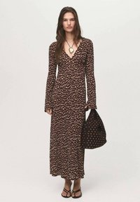 Robe maxi florale marron avec des manches longues, un décolleté en V et une silhouette fluide. Accordée avec un sac marron assorti avec des accents dorés.