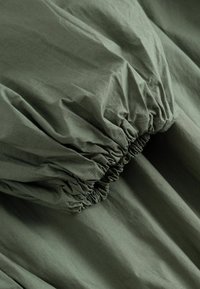Ύφασμα ελιάς με ελαστικό ριγωτό τελείωμα, που δείχνει την υφή και τις λεπτομέρειες ραφής.