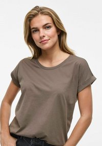 Camiseta marrón de manga corta hecha de algodón suave, con cuello redondo y puños enrollados, combinada con jeans de mezclilla oscuros.