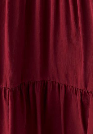 Bordo haljina s teksturiranim, složenim dizajnom. Ima glatki gornji deo i skupljene volane na dnu. Mekani, lagani materijal.