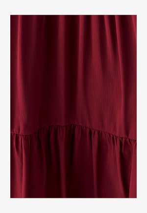 Bordo haljina s teksturiranim, složenim dizajnom. Ima glatki gornji deo i skupljene volane na dnu. Mekani, lagani materijal.