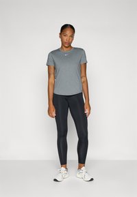 Camiseta atlética gris de manga corta y cuello redondo, combinada con leggings negros y zapatillas deportivas blancas con detalles en negro.