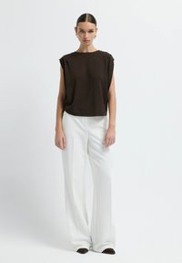 Bruine mouwloze top met een relaxte fit, gecombineerd met witte geklede broek, met een zachte textuur en een ingetogen ontwerp.