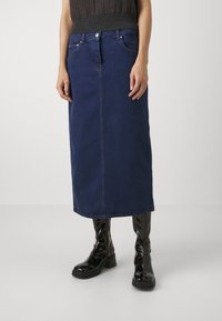 Tummansininen denim midi-hame, jossa on suora leikkaus, etutaskut ja erottuva ommel. Yhdistetty kiiltävämustiin polvipitkiin saappaisiin.