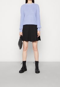 Suéter de punto lila claro con un diseño texturizado, combinado con una falda negra en línea A, botas de tobillo negras y un bolso negro acolchado.