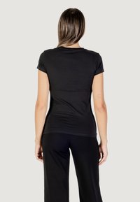Camiseta negra de manga corta ajustada, hecha de un textil suave, con un escote redondo y una textura lisa, combinada con pantalones negros holgados.