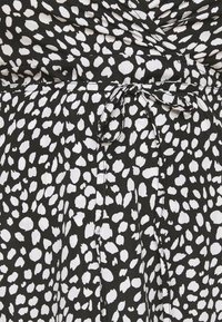 Czarnobiała sukienka w wzory, wykonana z lekkiego, teksturowanego materiału, z wiązaniem w talii i luźnym, zwiewnym krojem.