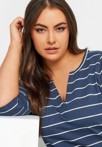 Navy sininen raidallinen paita, jossa valkoiset vaakasuorat raidat, V-pääntie, pehmeä kangas ja kolmanneksen pituiset hihat, mallin päällä.