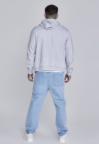 Szary hoodie z kieszenią kangurzą i kapturem na sznurki, w połączeniu z jasnoniebieskimi, luźnymi dżinsami. Strój ma swobodny krój i elastyczne mankiety.