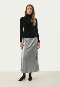Schwarzsamtes langärmliges Rollkragenhemd kombiniert mit einem silbernen Satin-Maxikleid. Das Outfit hat eine glatte Textur und eine figurbetonte Silhouette.