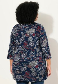 Marineblaue Bluse mit Dreiviertelärmeln. Verfügt über aufwendige Blumenmuster in Lila, Rot und Silber auf einem strukturierten Stoff.