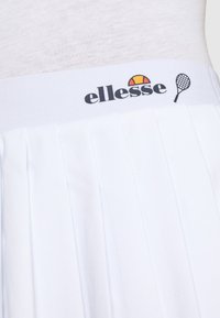 Gonna da tennis bianca plissettata con una ampia vita elastica decorata dal logo "ellesse" e una grafica di una racchetta da tennis stampata. Tessuto liscio.