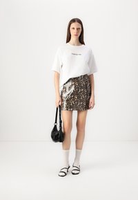 Witte T-shirt met korte mouwen en zwarte tekst, glanzende mini-jurk met luipaardprint, zwarte schoudertas, witte knie-sokken, zwarte schoenen met bandjes.
