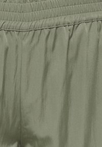 Tissu vert olive avec ceinture élastique, montrant une texture lisse et des coutures froncées en haut.
