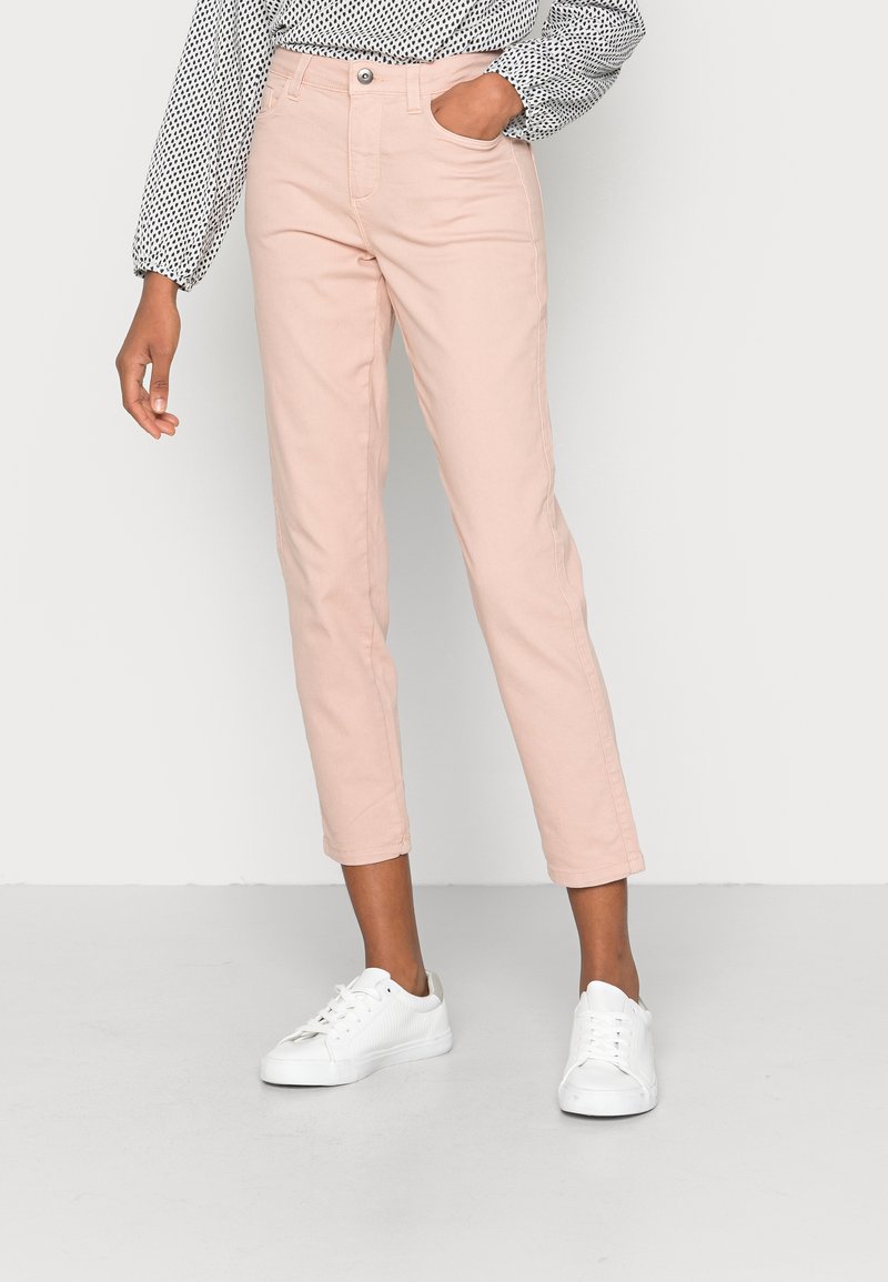 Pantalons rose clair, longueur cheville, avec une coupe classique, présentant des poches avant et une fermeture à bouton. Associés à des baskets blanches.