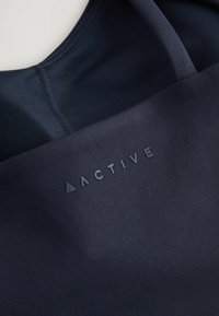 Donker marineblauw sporttop met een gladde textuur, voorzien van een verhoogd "ACTIVE" logo in zwart. Minimalistisch ontwerp, ronde halslijn en platte naden.