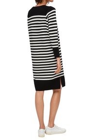 Gestre knitted Kleid in Schwarz und Weiß mit langen Ärmeln, seitlichen Schlitzen und einem einfarbigen schwarzen Rücken. Stilisiert mit weißen Sneakern.