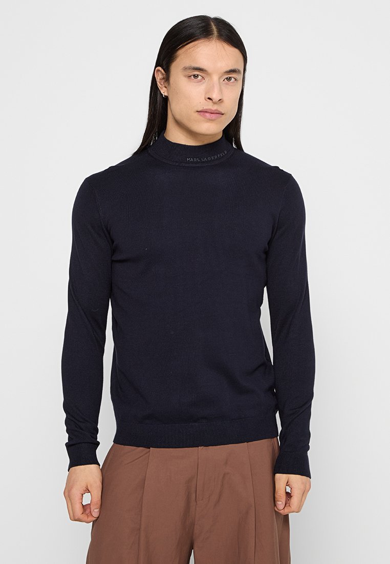 Dunkelblauer Rollkragenpullover aus geripptem Strickmaterial mit langen Ärmeln. Mit einem dezenten Logo-Detail in der Nähe des Ausschnitts. Regelmäßige Passform.