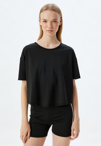 Mustapaitainen cropped t-paita, joka on valmistettu sileästä kankaasta, jossa on pyöreä kaula-aukko ja lyhyet hihat, yhdistettynä mustiin tiukkaan istuviin shortseihin.