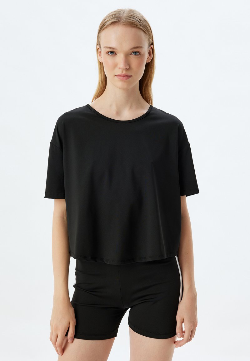 Mustapaitainen cropped t-paita, joka on valmistettu sileästä kankaasta, jossa on pyöreä kaula-aukko ja lyhyet hihat, yhdistettynä mustiin tiukkaan istuviin shortseihin.