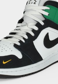 Μαύρο, άσπρο και πράσινο Nike Air αθλητικό παπούτσι με λευκές κορδόνια, μαύρο λογότυπο swoosh και μικρό κίτρινο swoosh στην περιοχή των δαχτύλων, κοντινή όψη.