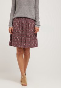 Vínová sukně s potiskem a skládacím pasem, zdobená květinovými a paisley vzory. Spárována se šedým pleteným svetrem a béžovými sandály na otevřenou špičku.